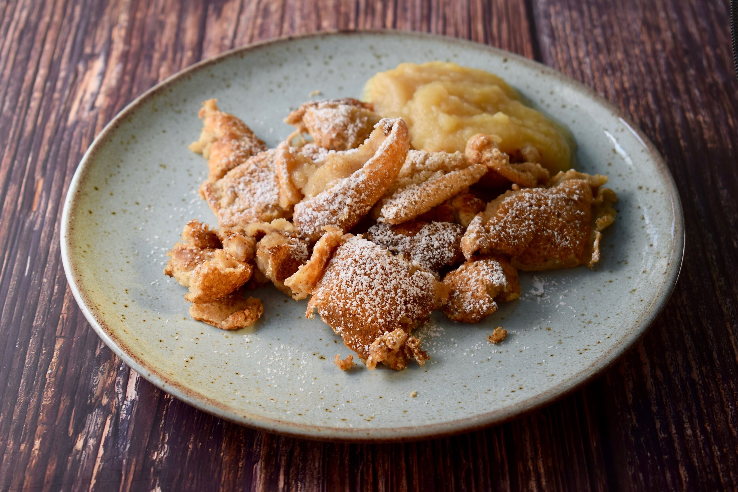 Schöner hellblauer Teller mit Kaiserschmarrn und Apfelmus auf Holztisch