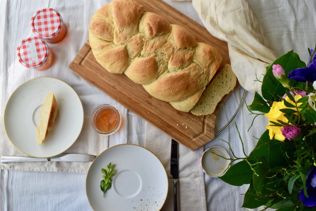 Schön gedeckter Tisch mit Hefezopf in der Mitte, einem frühlingshaftem Blumenstrauß und zwei Tellern