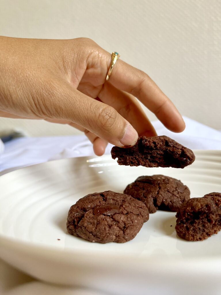 weißer Teller mit Schokocookies und eine Hand, die sich gerade ein Stück davon nimmt 