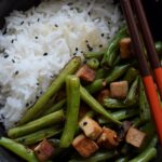 Nahaufnahme der Buschbohnen mit Räuchertofu auf Reis mit schwarzem Sesam